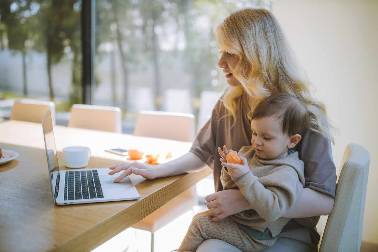 Frau, die ihr Baby trägt und an einem Laptop arbeitet