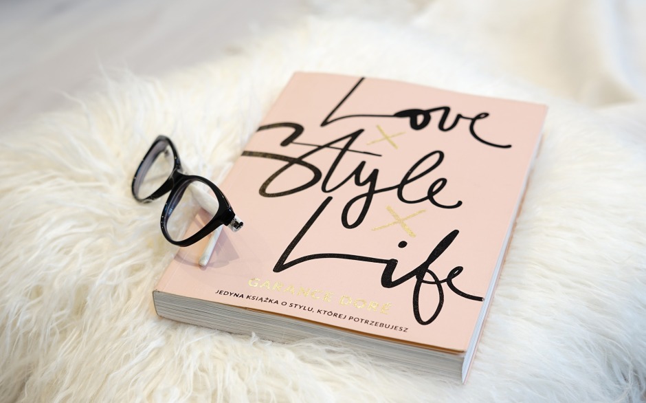 Ein Buch mit dem Titel 'Love Style Life' liegt auf einem Schaffellteppich, daneben liegt eine Brille