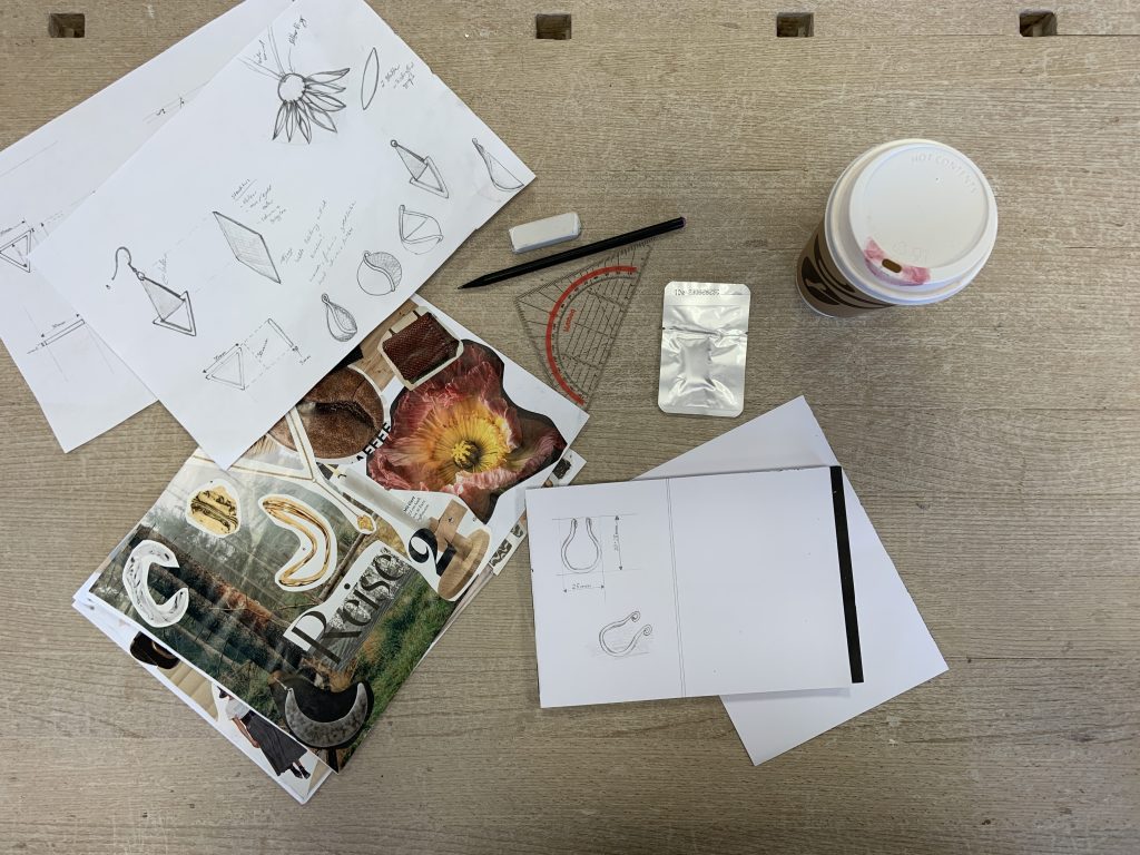 Das Bild zeigt eine von oben aufgenommen Arbeitsfläche auf der neben einem Kaffeebecher unterschiedliche Dokumente mit Zeichnungen und ausgeschnittenen Bildern zur Inspiration liegen. 